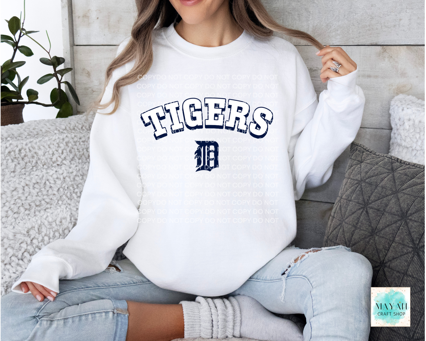 Person wearing a white sweatshirt with baseball logo printed on it, sitting on a couch.