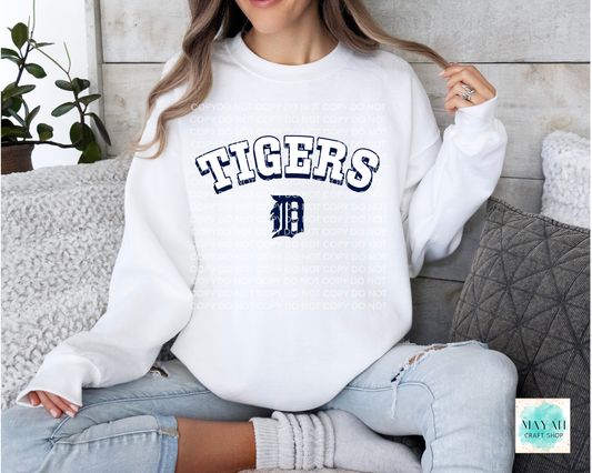 Person wearing a white sweatshirt with baseball logo printed on it, sitting on a couch.