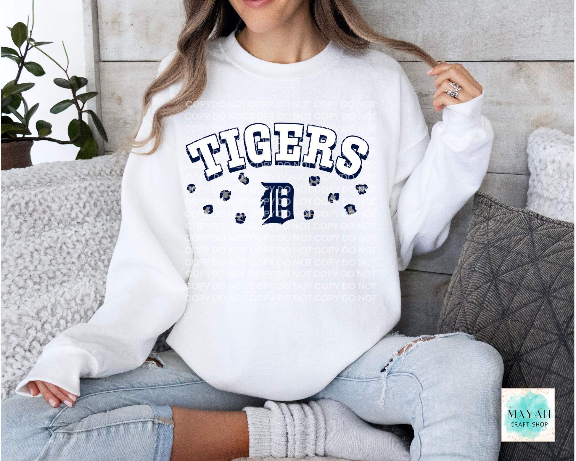 Person wearing a white sweatshirt with baseball logo printed on it, sitting on a couch.