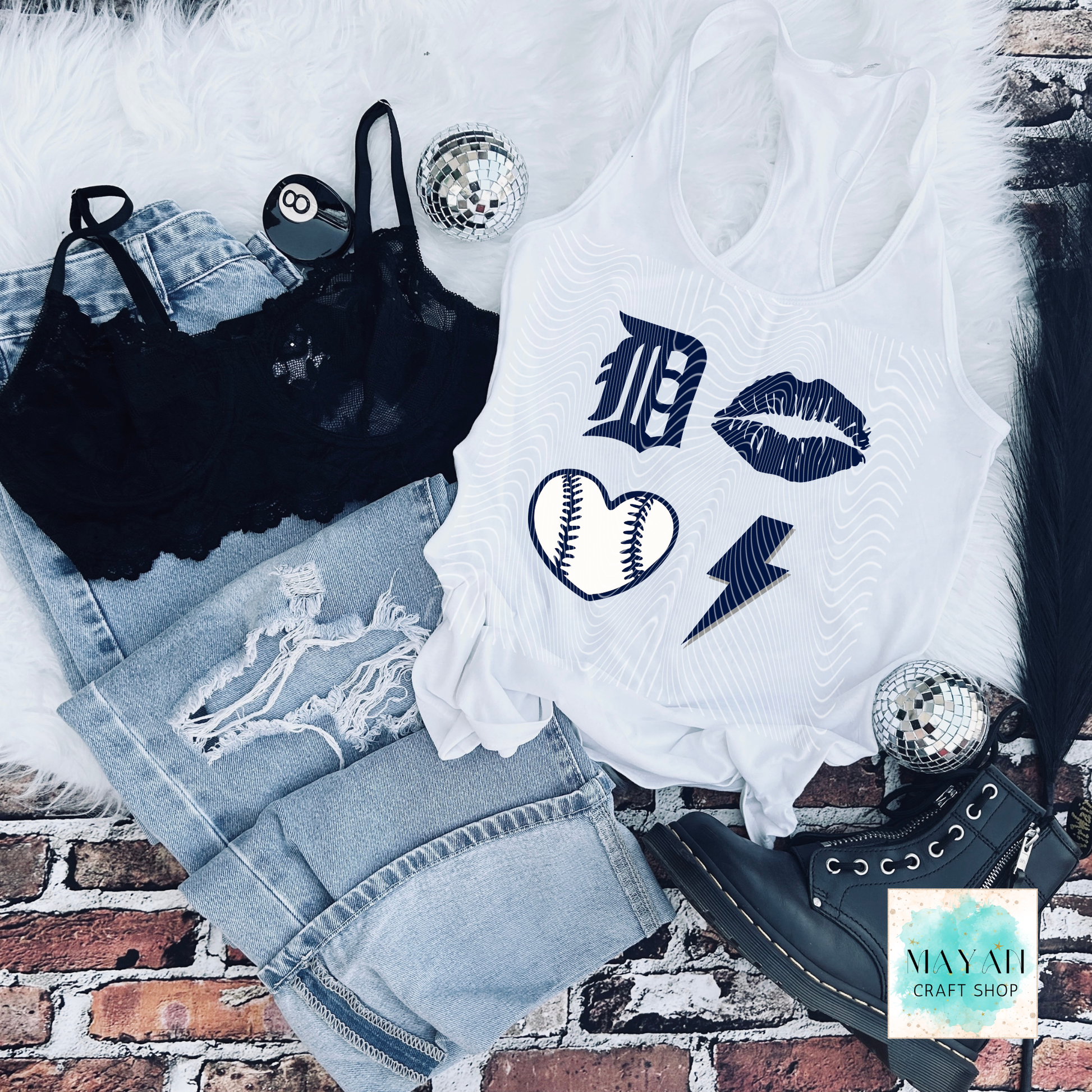 White tank top with graphic designs on a brick surface, surrounded by denim shorts and black lace top.