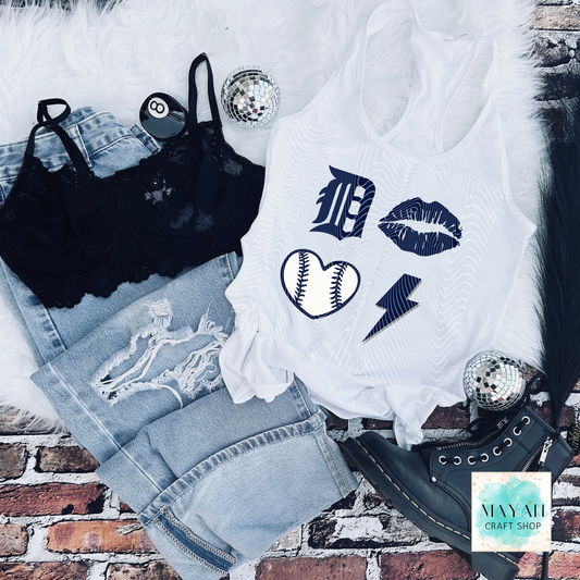 White tank top with graphic designs on a brick surface, surrounded by denim shorts and black lace top.