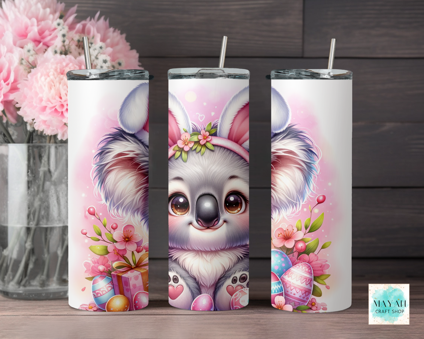 Three tumbler with a cute koala design on a wooden surface with flowers in the background.