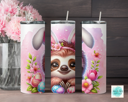 Three tumbler with sloth design wearing bunny ears on a wooden surface with pink flowers in the background.