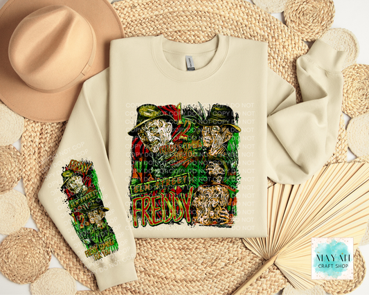 A cream-colored crewneck sweatshirt featuring a detailed graphic print. The sweatshirt is displayed in a styled flat-lay arrangement with a beige fedora hat, a woven mat, and a paper fan.