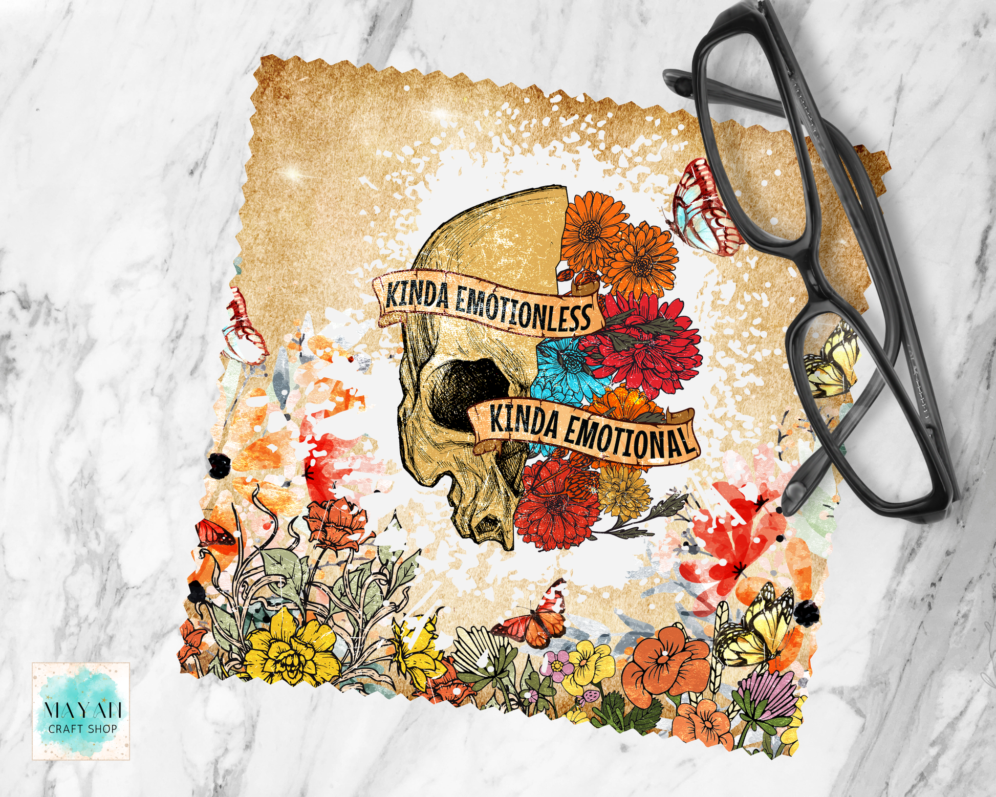 A lens cloth cleaner with a distressed beige background, featuring a central skull illustration surrounded by colorful flowers and butterflies. Two tan banners across the skull read 'KINDA EMOTIONLESS' and 'KINDA EMOTIONAL.