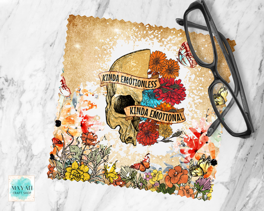 A lens cloth cleaner with a distressed beige background, featuring a central skull illustration surrounded by colorful flowers and butterflies. Two tan banners across the skull read 'KINDA EMOTIONLESS' and 'KINDA EMOTIONAL.