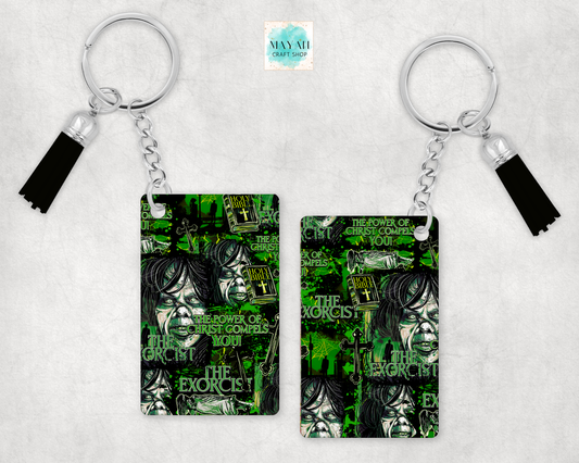 Two keychains with black tassels, featuring a green and black graphic print, displayed on a light gray textured background.