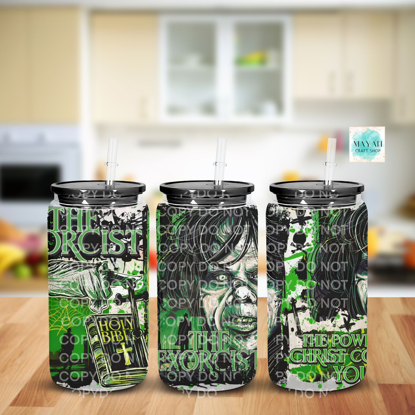 Three frosted insulated tumblers with black lids and clear straws, shown on a wooden surface with a blurred kitchen background. The tumblers feature a green and black graphic design.