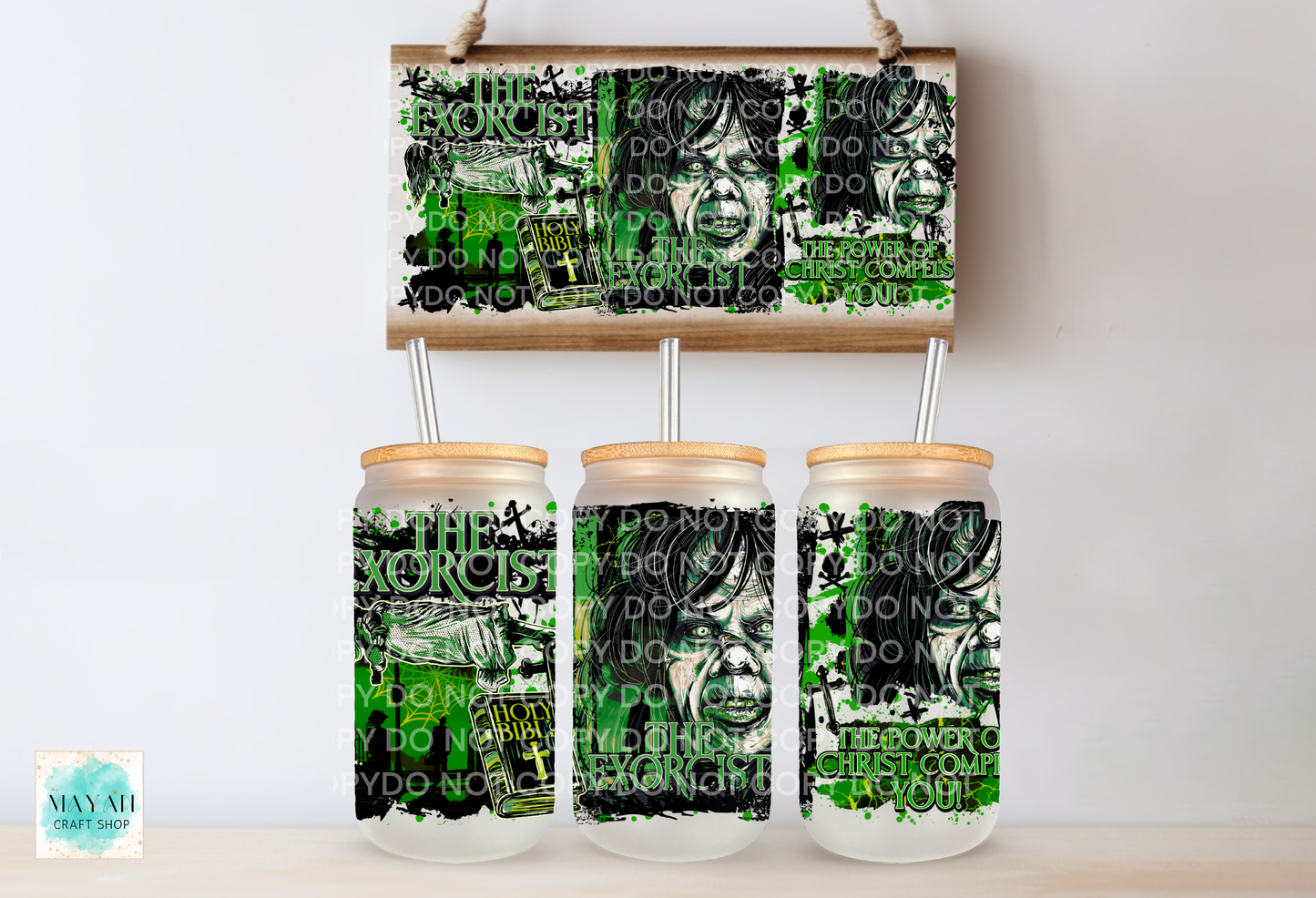 Three clear glass mason jar tumblers with bamboo lids and metal straws, printed with a black, white, and green graphic design. A matching rectangular print is displayed above them on a wooden hanger against a white wall.