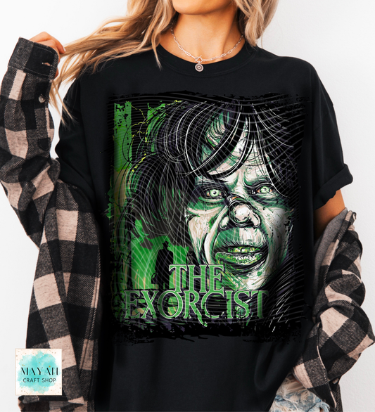A woman wearing a black graphic t-shirt featuring a stylized green and white illustration of a character with the title printed below. She is wearing a black and white plaid flannel shirt as an overlay.