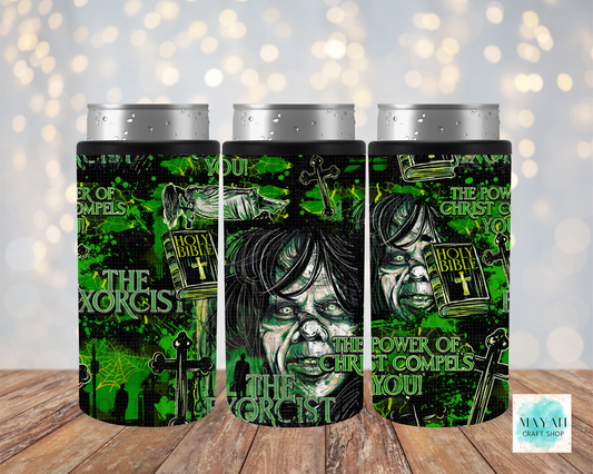 Three slim can coolers with silver aluminum cans inserted, displayed on a wooden surface against a soft bokeh background. The coolers feature a green and black gothic horror design along with illustrations of a demon face, a Bible, and a cross.