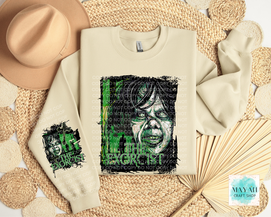 A cream-colored sweatshirt with a green and black graphic print of a face, styled in a flat lay with a tan hat, woven mat, and paper fan.
