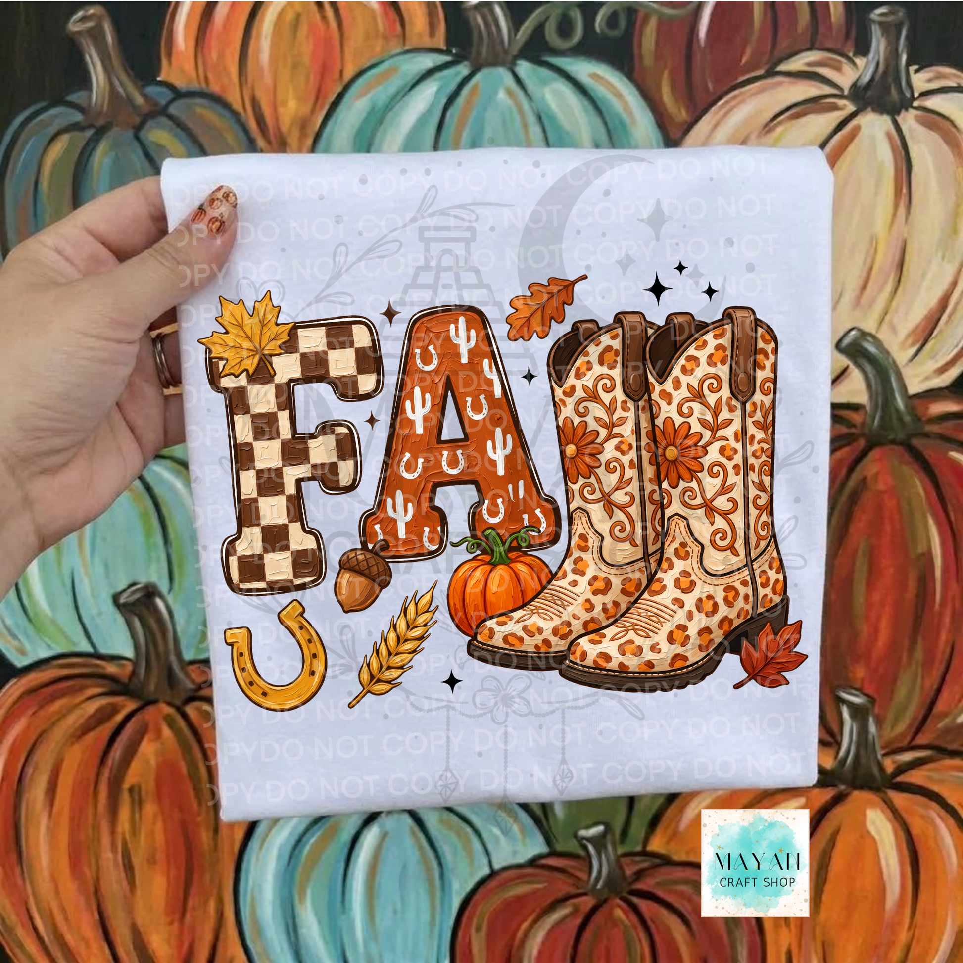 A hand holds a white t-shirt featuring a western-themed 'FALL' graphic with autumn and cowboy boot illustrations, set against a painted background of pumpkins. 