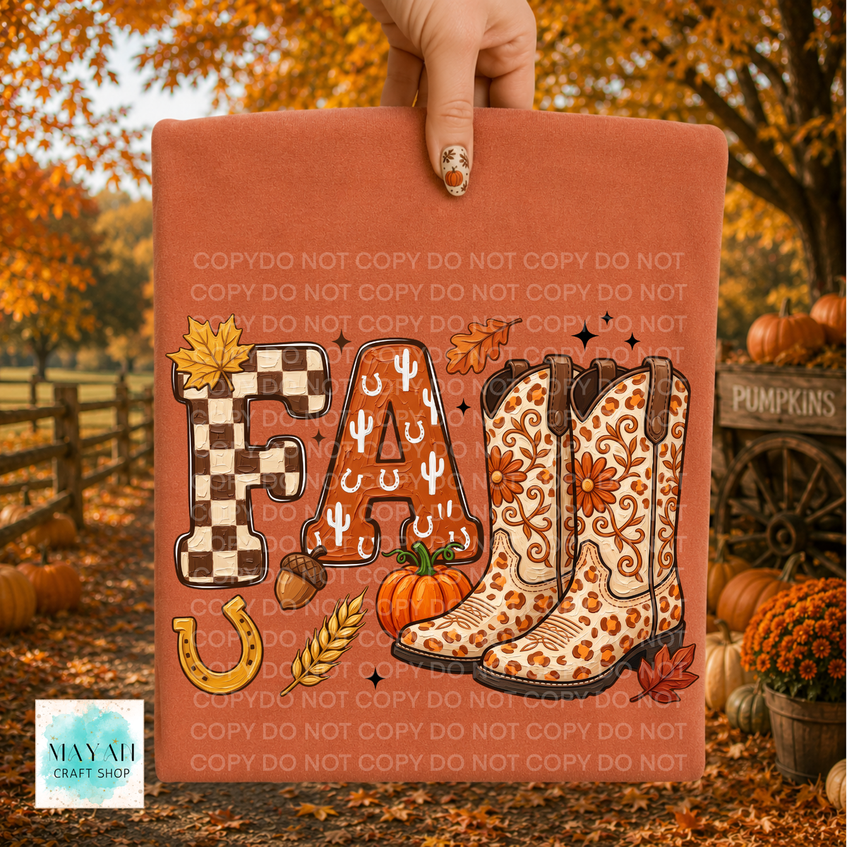 A terracotta-colored fall-themed graphic print held up by a hand, featuring the word 'FALL' in decorative block letters with western boots, pumpkins, acorns, and a horseshoe. The background shows an autumn outdoor scene with pumpkins and fall foliage.