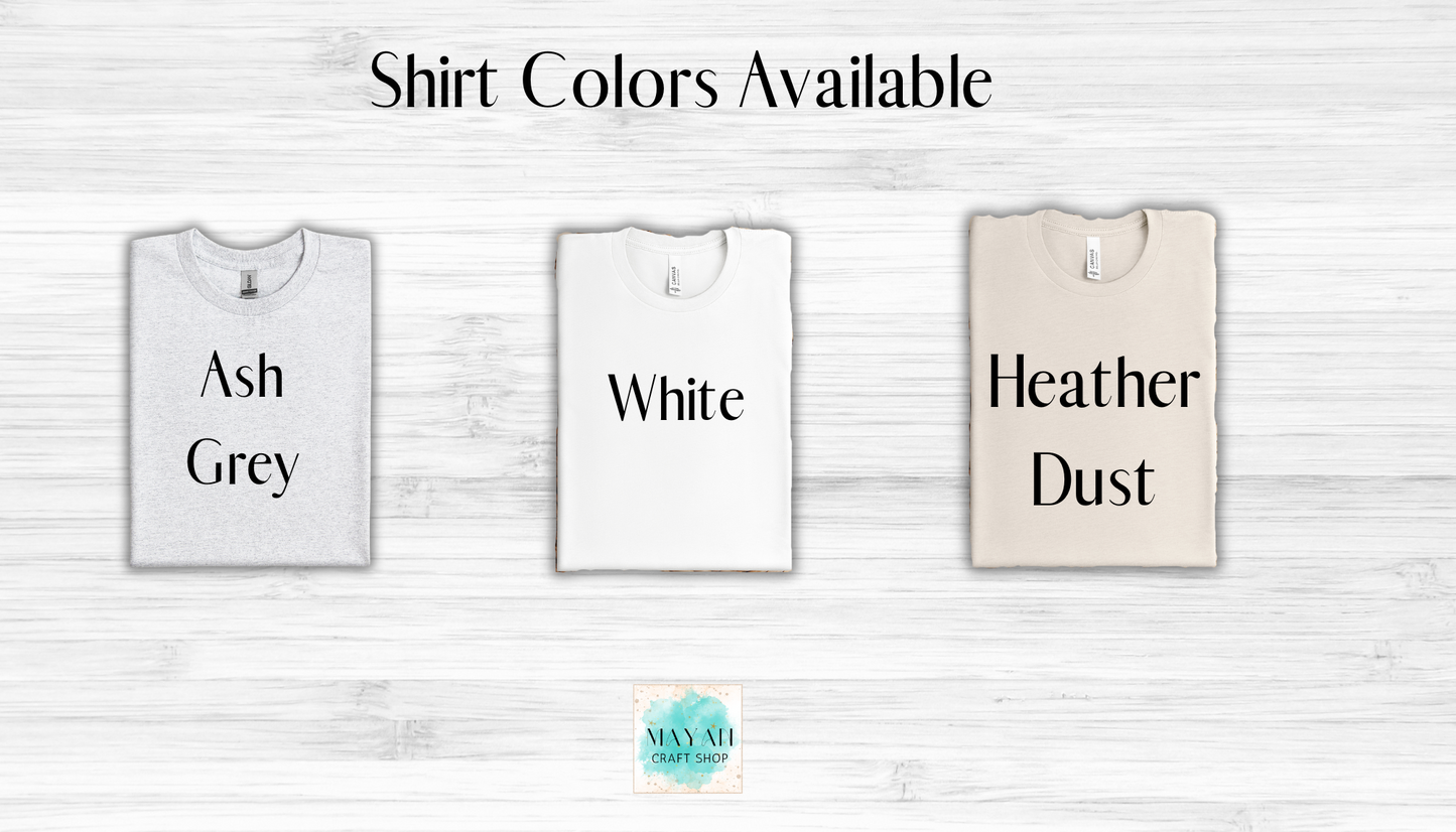 Three t-shirts in ash grey, white, and heather dust with color options displayed on a light wooden background.