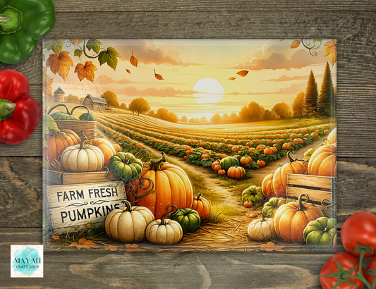 A cutting board featuring an autumn farm field with rows of pumpkins and gourds, a sunset sky, and a sign reading 'FARM FRESH PUMPKINS.' The sign is photographed on a rustic wood surface with decorative red and green peppers around it.