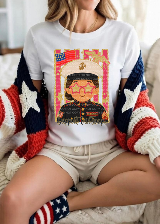 A woman wearing a white graphic t-shirt with a military-themed patriotic print, styled with a red, white, and blue knit cardigan and beige shorts.