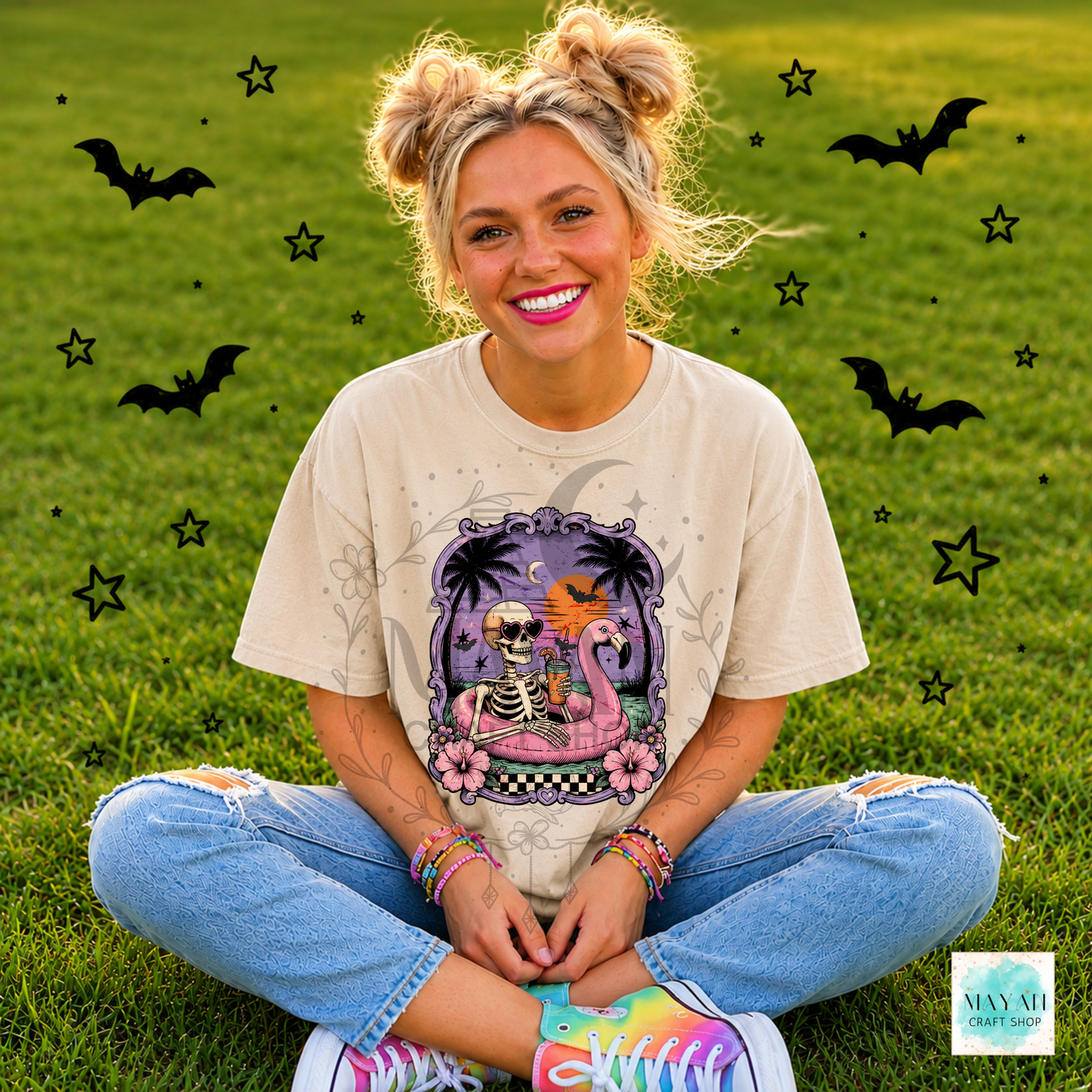 Person sitting on grass wearing a Halloween-themed t-shirt with decorative elements.