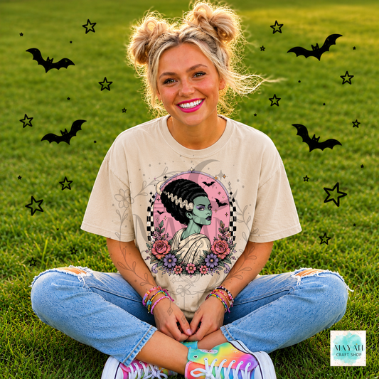 Person sitting on grass wearing a t-shirt with a graphic design, surrounded by decorative elements like bats and stars.