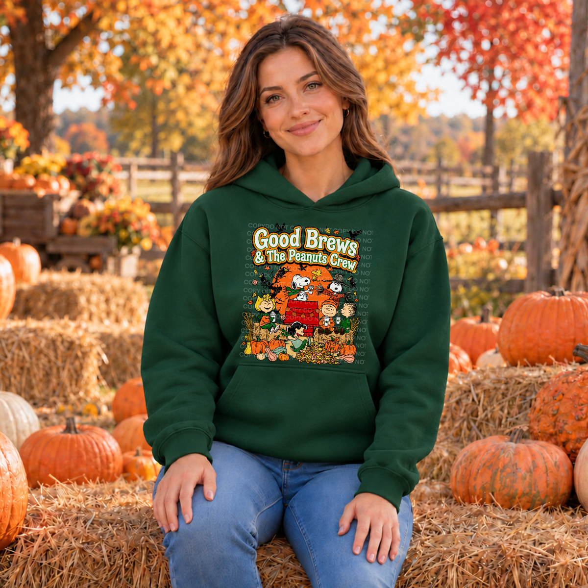 A woman wearing a forest green hoodie with a 'Good Brews' graphic sits on a hay bale in an autumn pumpkin patch.