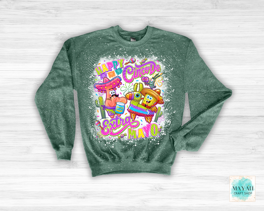 Green sweatshirt with cartoon characters and colorful text on a white wooden background