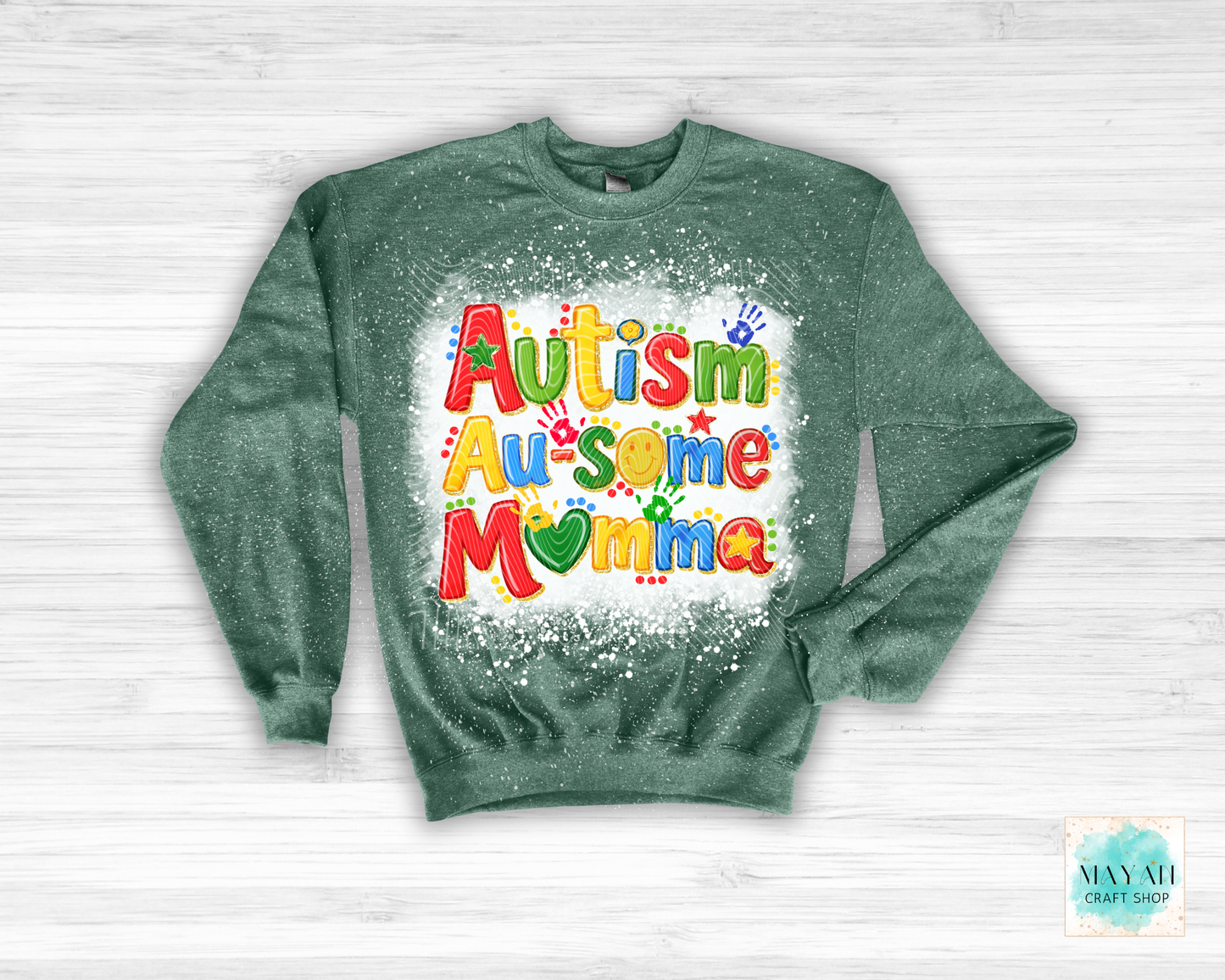 Green sweatshirt with colorful 'Autism Au-some Momma' text on a white wooden background