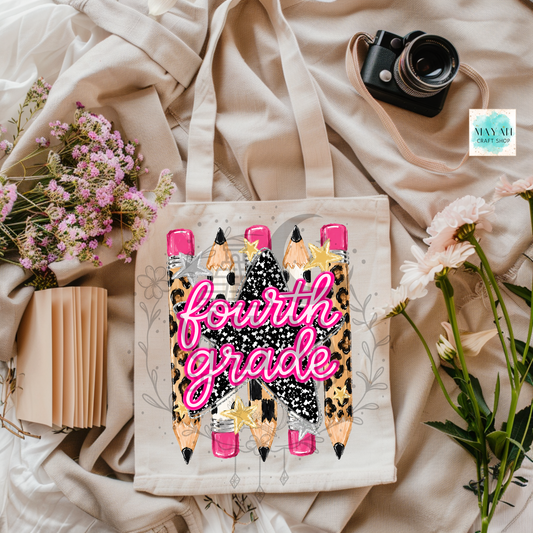 A canvas tote bag with a 'fourth grade' school-themed graphic featuring cartoon pencils and leopard print, styled in a flat lay with flowers, a camera, and a notebook on beige fabric.