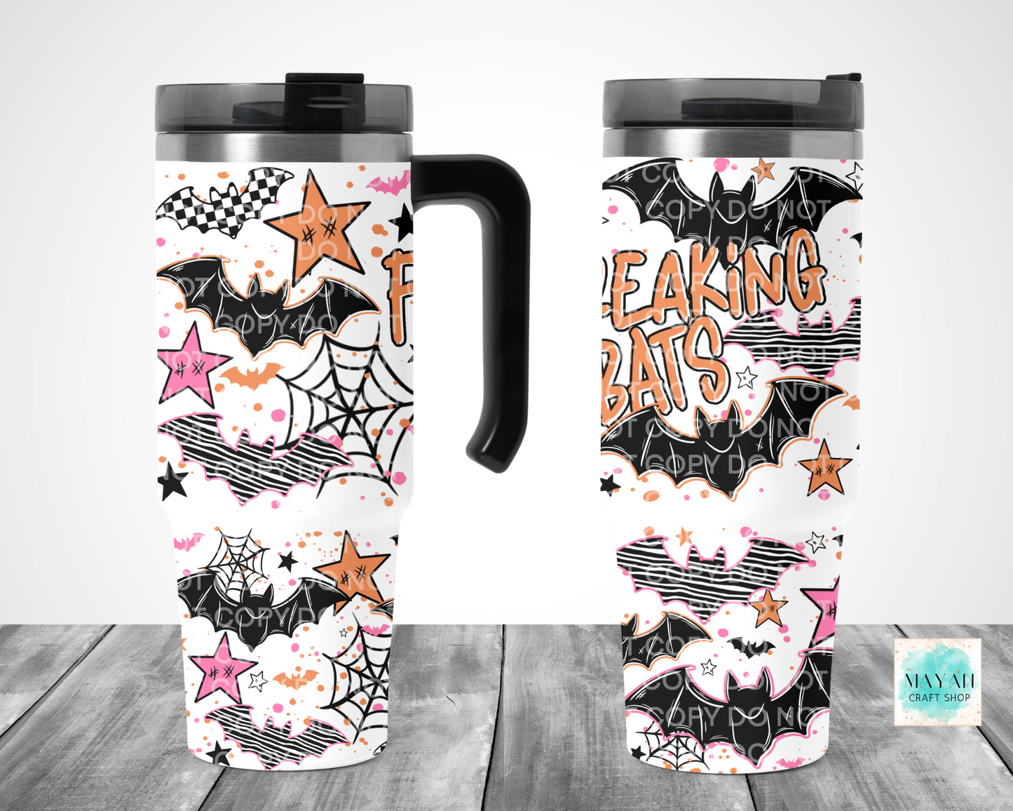 Two views of a travel tumbler with a Halloween-themed 'Freaking Bats' print, featuring black bats, pink and orange stars, spiderwebs, and comic-style stripes on a white background, displayed on a gray wood surface.
