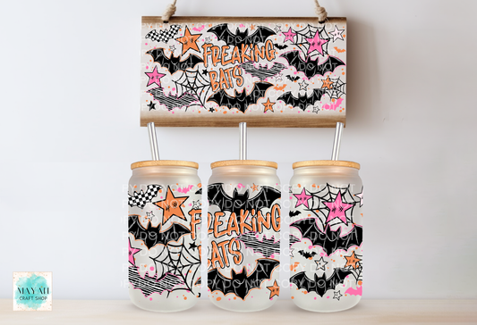 Three frosted glass mason jars with bamboo lids and metal straws, decorated with a black, white, pink, and orange 'Freaking Bats' Halloween pattern, displayed below a matching rectangular sign on a light wood surface against a white wall.