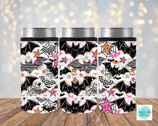 Three slim can coolers with a Halloween-themed pattern featuring bats, spiders, webs, stars, and pink clouds, shown on silver aluminum cans against a blurred warm bokeh background and wood surface.