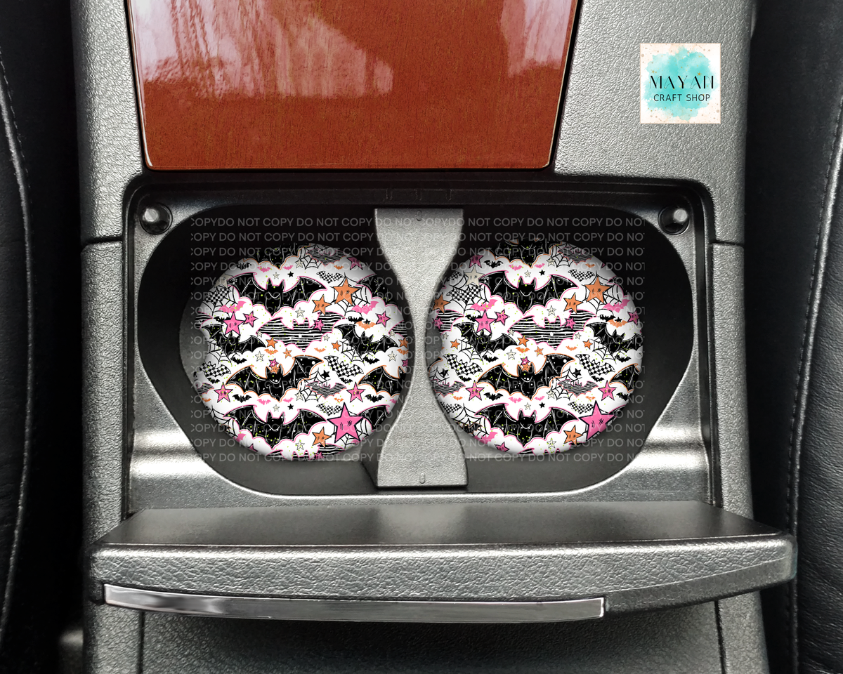 A pair of circular car cup holders with a black, white, and pink bat-and-flower pattern, installed in a gray car console.
