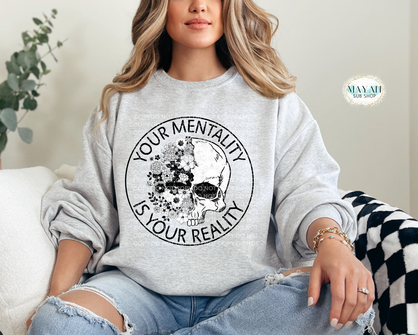 Person wearing a gray sweatshirt with a skull design and text, sitting on a couch.