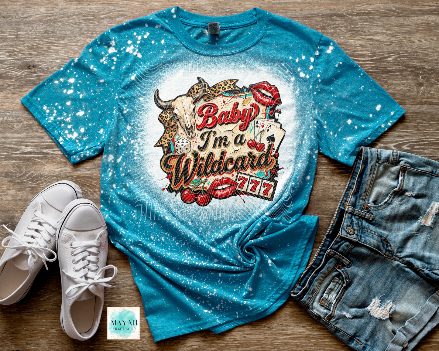 Blue t-shirt with graphic design and text, paired with white sneakers and denim shorts on a wooden surface.
