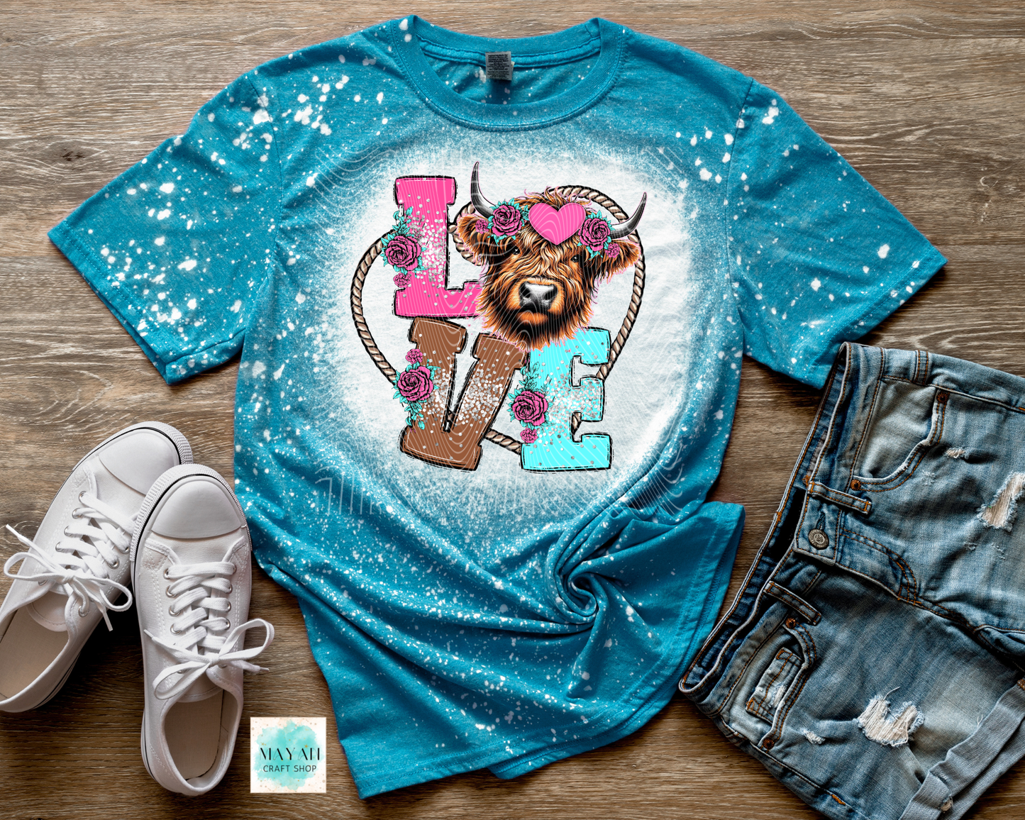 Blue t-shirt with a graphic design of a lion and floral elements on a wooden surface with white sneakers and denim shorts.