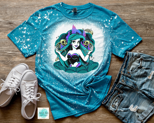 Blue bleached t-shirt with a mermaid graphic, white sneakers, and denim shorts on a wooden surface.