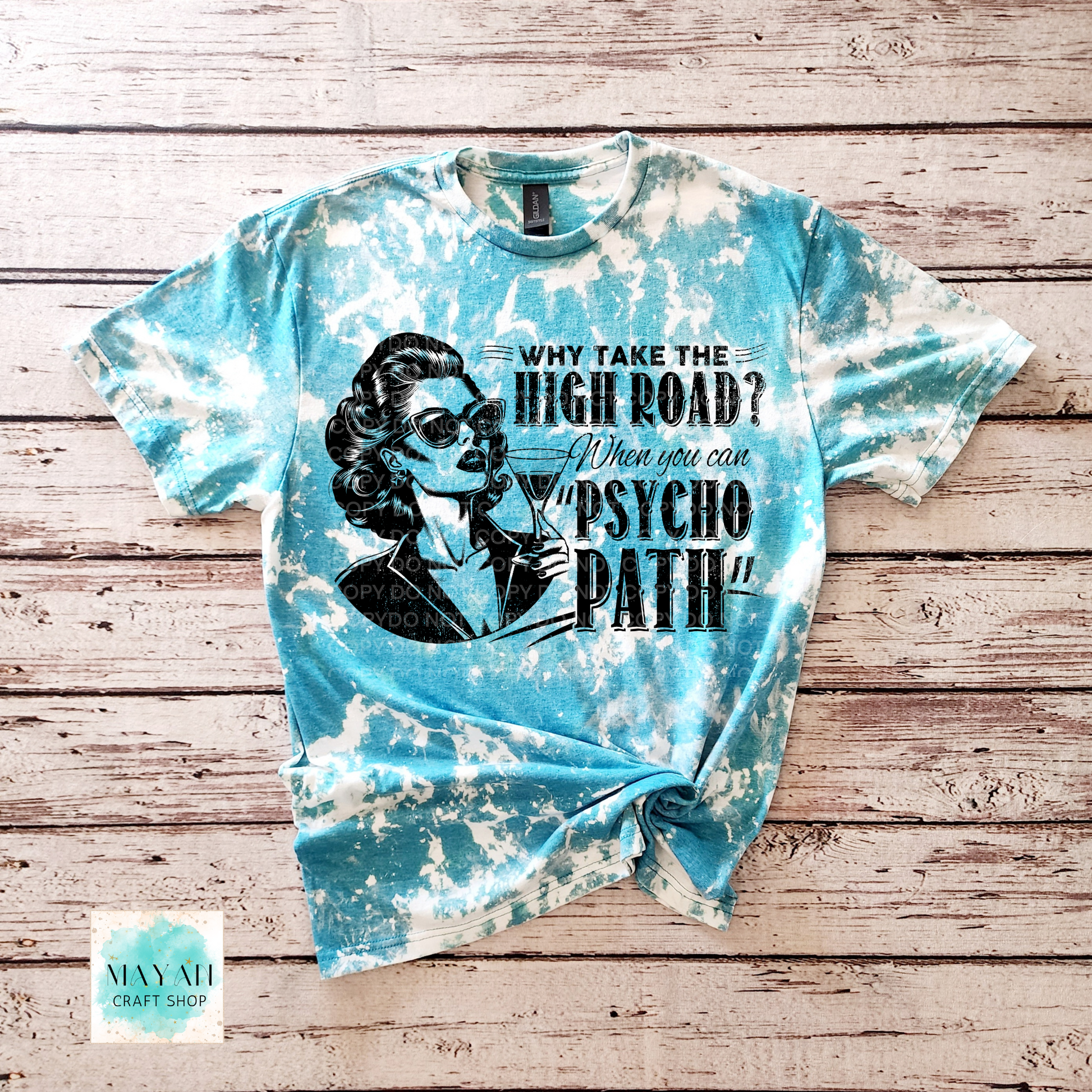 Tie-dye t-shirt with graphic design and text on a wooden surface, featuring the brand 'Mayan Craft Shop'.