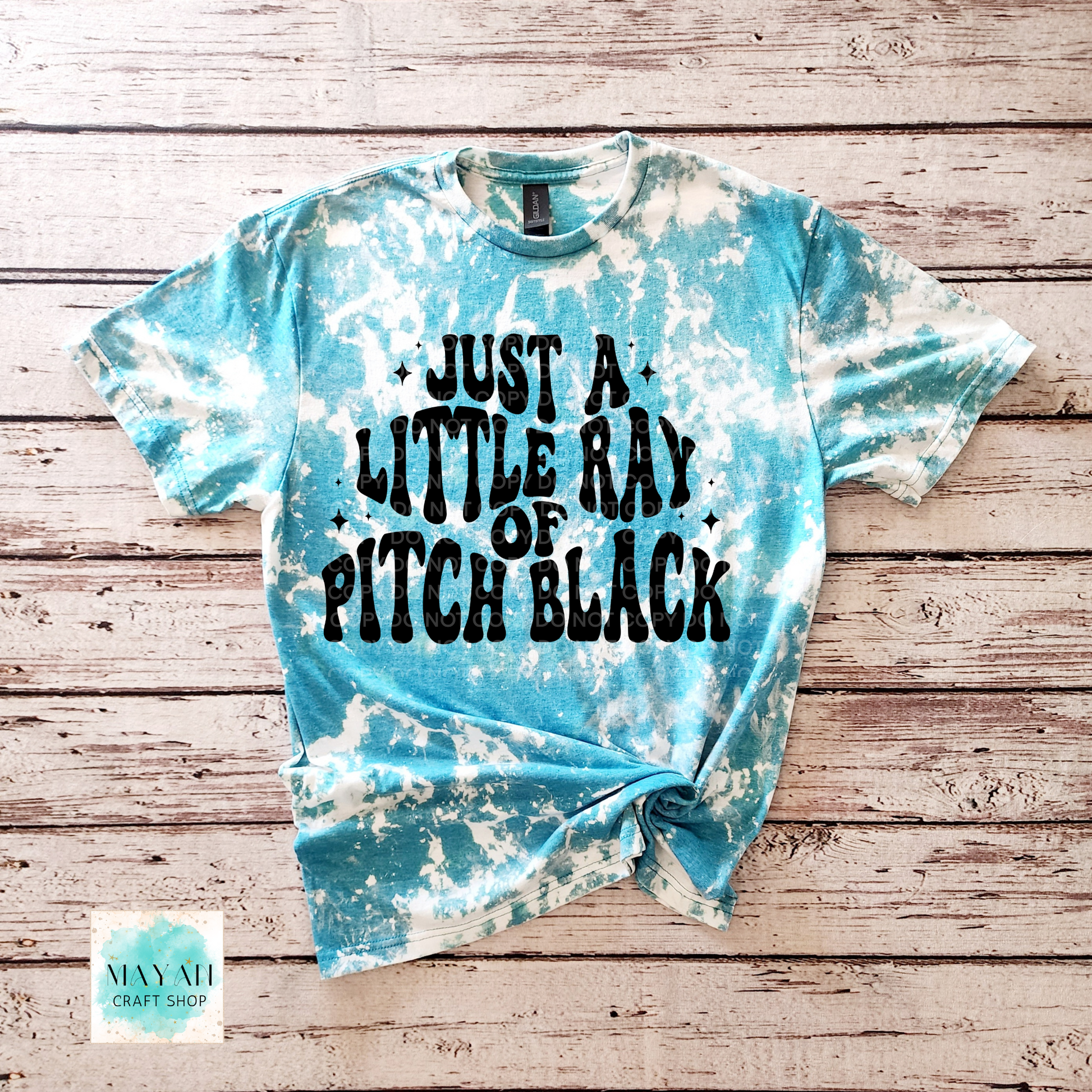 Tie-dye t-shirt with text on a wooden surface, featuring the brand 'Mayan Craft Shop'.