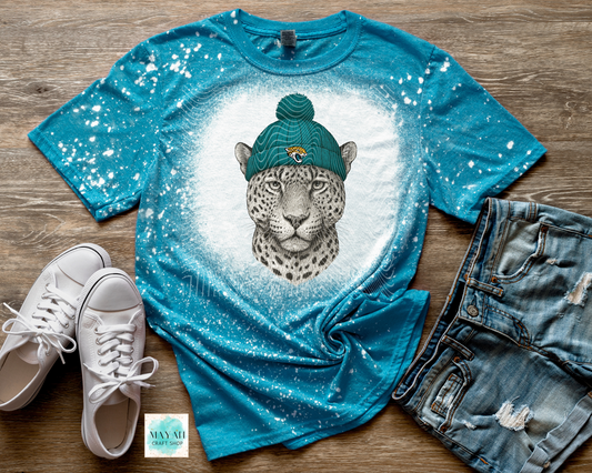 Blue t-shirt with a leopard graphic and text, paired with white sneakers and denim shorts on a wooden surface.