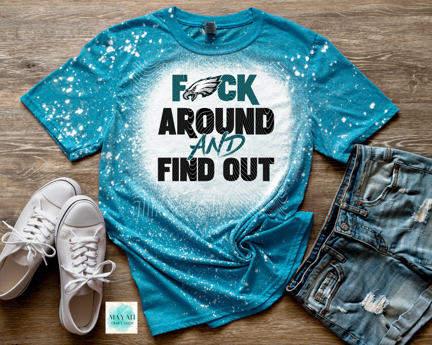 Blue t-shirt with graphic design and text on a wooden surface with shoes and shorts.