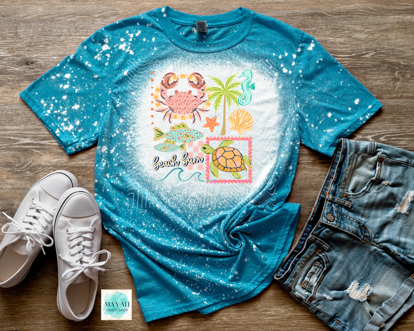 Blue t-shirt with beach-themed design on a wooden surface with white sneakers and denim shorts.