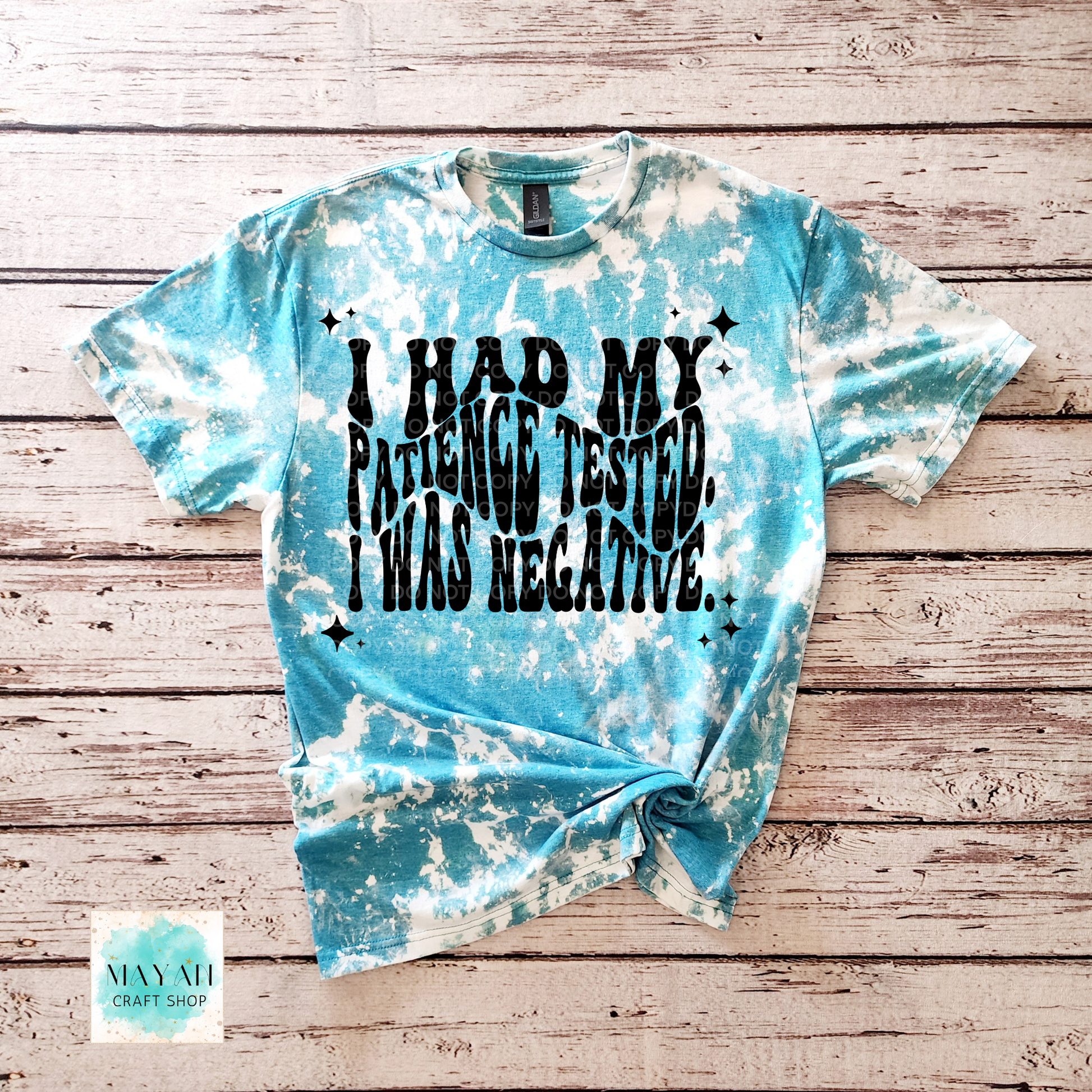 Blue tie-dye t-shirt with text on a wooden surface, featuring the brand 'Mayan Craft Shop'.
