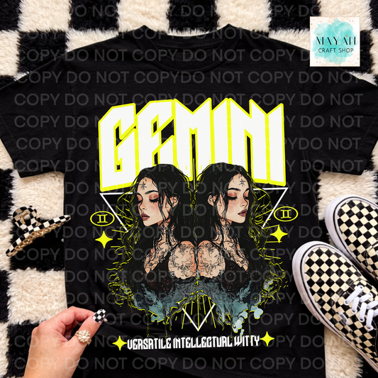 A black graphic t-shirt featuring a Gemini-themed design with two illustrated women, neon yellow 'GEMINI' text, and the phrase 'VERSATILE INTELLIGENT WITTY'. The shirt is displayed in a flat-lay arrangement on a black and white checkered rug, next to sneakers and a hand holding a checkered accessory.