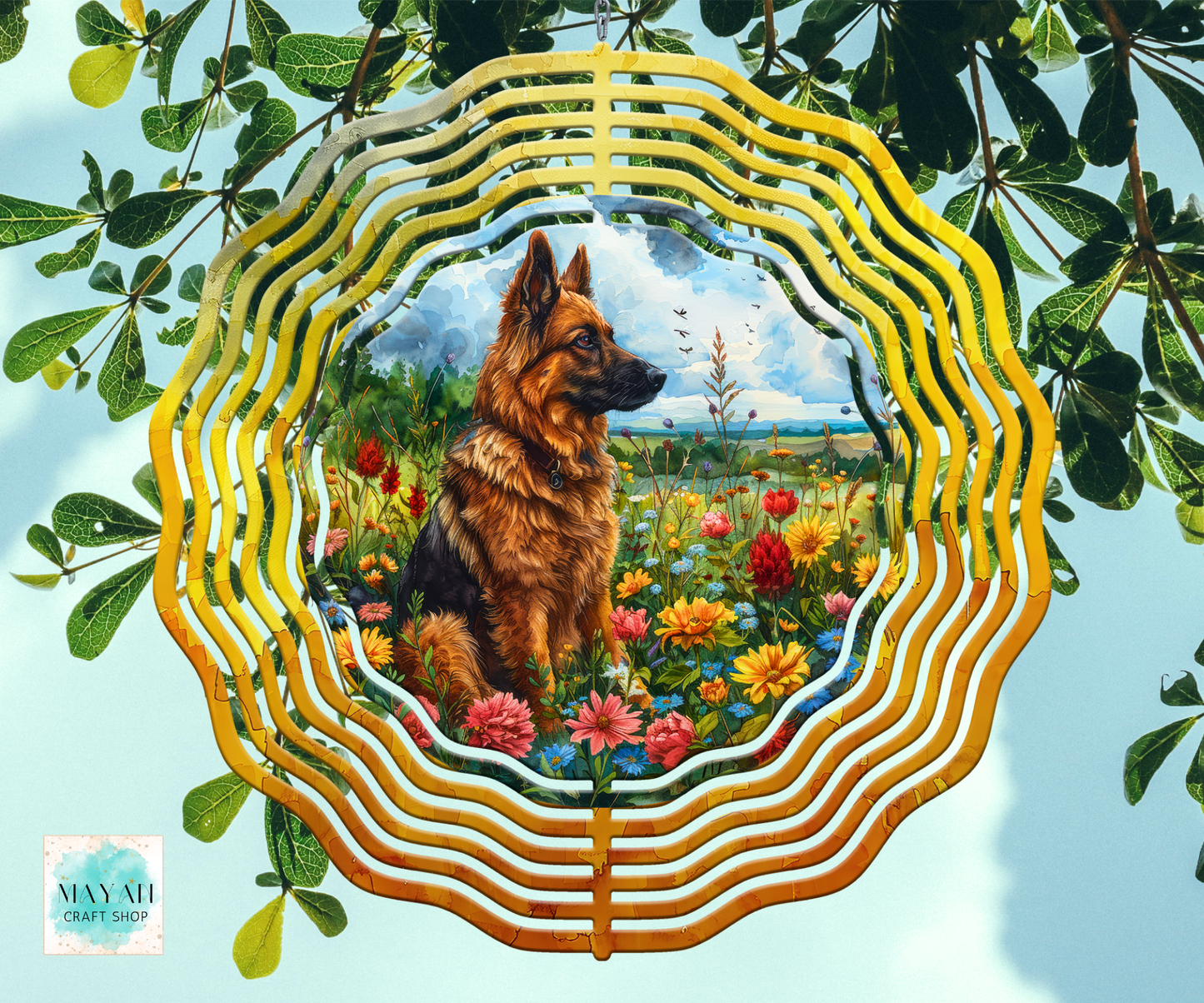 A wind spinner hanging with a colorful illustration of a German Shepherd dog sitting in a flower field, surrounded by layered gold, yellow, and white concentric rings, shown against a light blue sky background with green leaves.