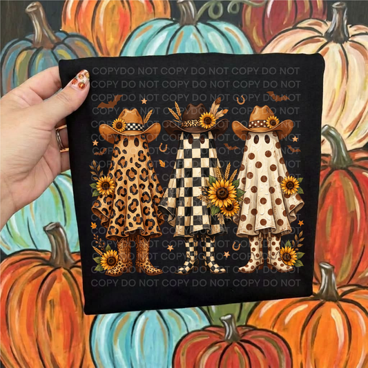 A hand holds a black shirt featuring three autumn-themed outfits: leopard print, black and white checkered, and beige with brown polka dots, decorated with sunflowers, hats, and boots. The background is a colorful painted pumpkin scene.