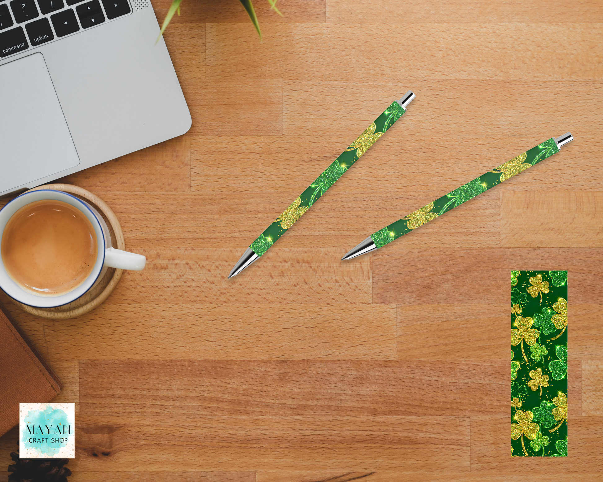 Two green pens with floral design on a wooden desk with a laptop and coffee cup.