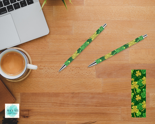 Two green pens with floral design on a wooden desk with a laptop and coffee cup.