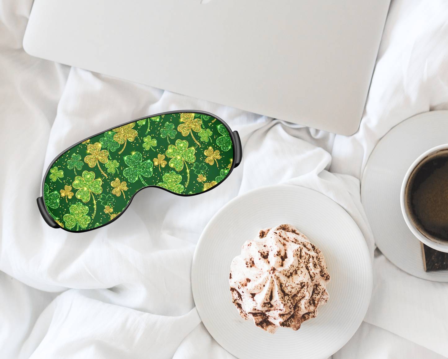 Green shamrock patterned eye mask on a white surface with a cup of coffee and dessert.