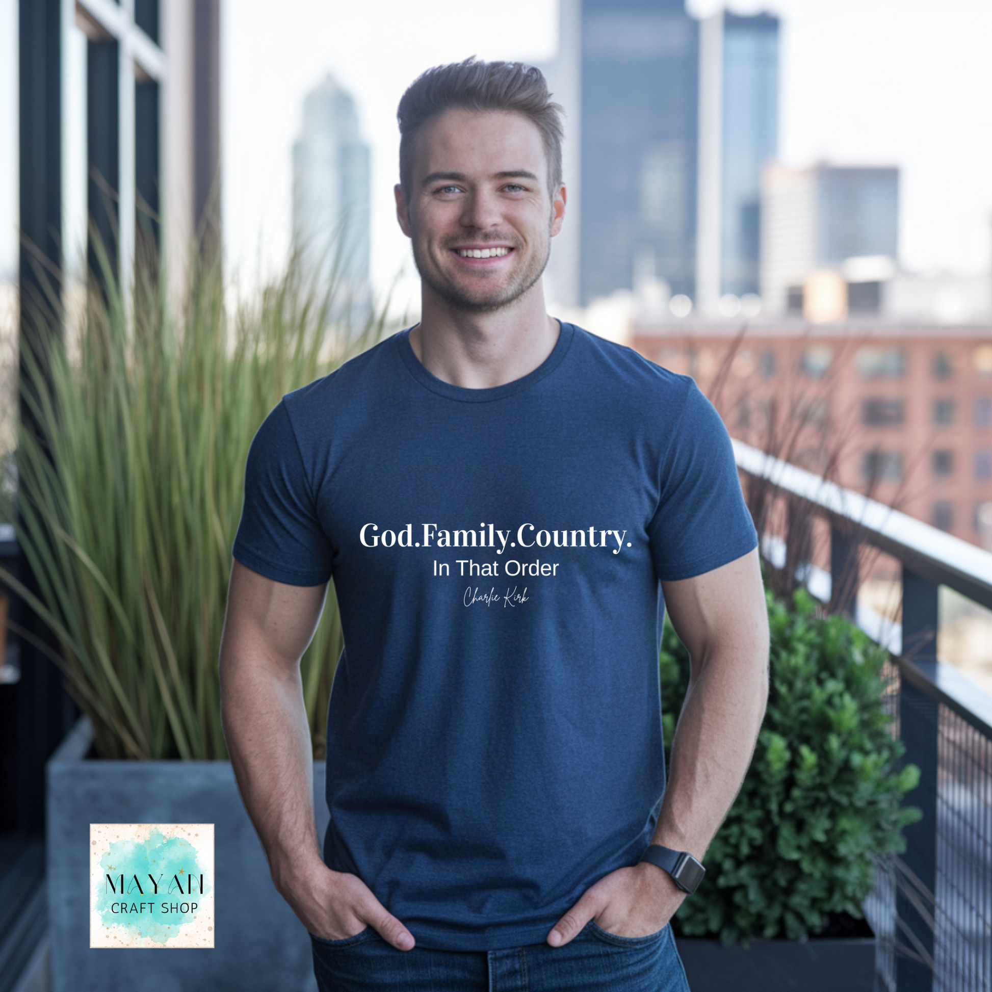 Man wearing a navy blue t-shirt with text, standing on a balcony with cityscape in the background.