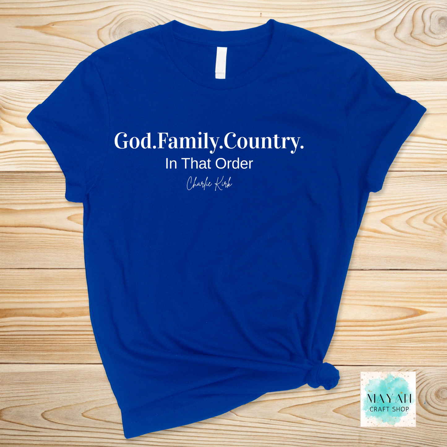 Blue t-shirt with text 'God. Family. Country. In That Order' on a wooden surface, with a brand logo in the corner.
