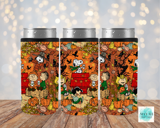 Three insulated can coolers with silver metal can tops, featuring a colorful autumn-themed Peanuts print with pumpkins and characters on a wooden surface against a blurred bokeh background.